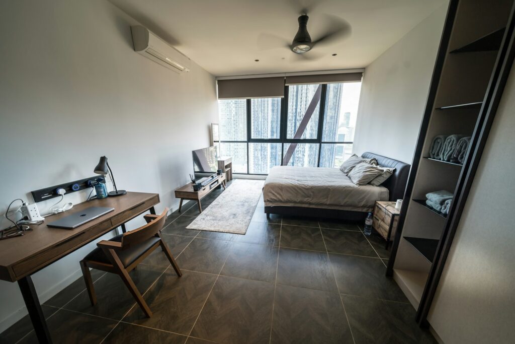 Modern studio apartment with a wooden desk, laptop and made bed, and a city skyline outside
